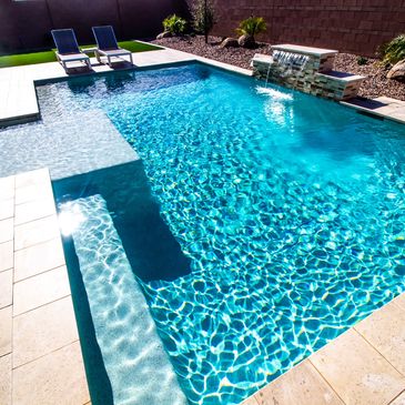 A bright outdoor swimming pool with clear blue water and lounge chairs.